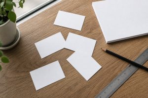 Beberapa kartu nama polos di atas meja kayu dengan penggaris dan pensil sebagai contoh pengaturan tata letak